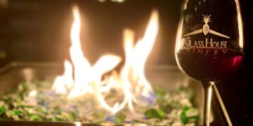 A glass of wine at Glass House Winery sits on a table in front of the fire pit