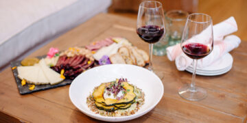 Two glasses of wine featured on the tour, next to a plate of food and a charcuterie board